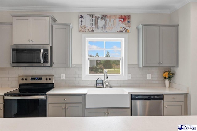 kitchen featuring tasteful backsplash, light countertops, appliances with stainless steel finishes, ornamental molding, and a sink
