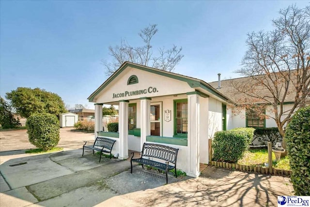 view of front facade featuring a porch, an outbuilding, stucco siding, and a shed