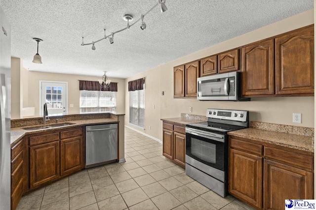 kitchen featuring light tile patterned flooring, appliances with stainless steel finishes, decorative light fixtures, sink, and a textured ceiling