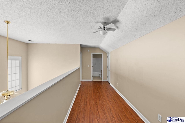 hallway with lofted ceiling, hardwood / wood-style floors, and a textured ceiling