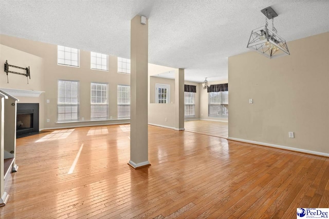 unfurnished living room featuring a chandelier, a textured ceiling, and light wood-type flooring