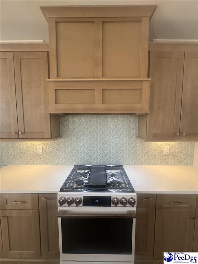 kitchen featuring stainless steel gas stove, backsplash, and light stone countertops