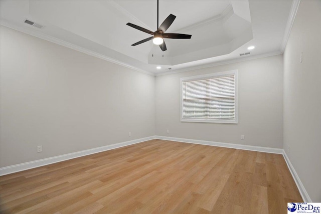 spare room with a tray ceiling, light wood-style flooring, and baseboards