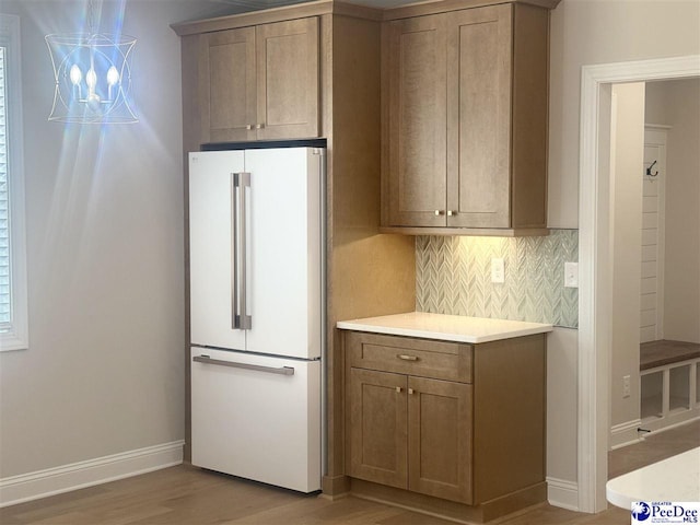 kitchen featuring baseboards, light countertops, light wood-type flooring, backsplash, and freestanding refrigerator