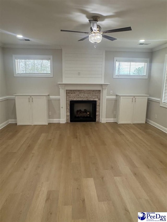 unfurnished living room featuring a fireplace, crown molding, visible vents, light wood-style flooring, and baseboards