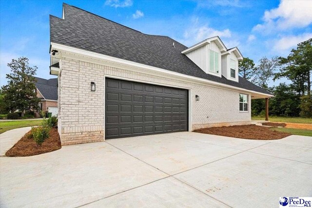 view of property exterior featuring a shingled roof, concrete driveway, brick siding, and an attached garage