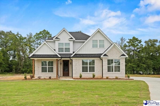 craftsman inspired home featuring a shingled roof, a front yard, and brick siding