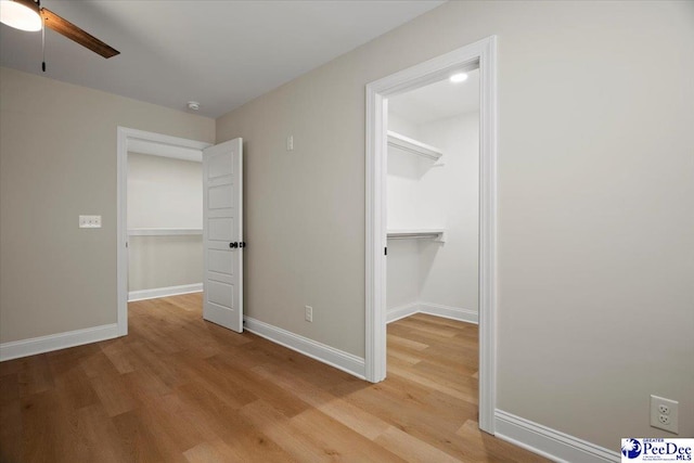 unfurnished bedroom with light wood finished floors, baseboards, and a walk in closet