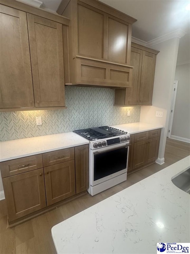 kitchen with light stone counters, light wood-style floors, backsplash, gas stove, and crown molding