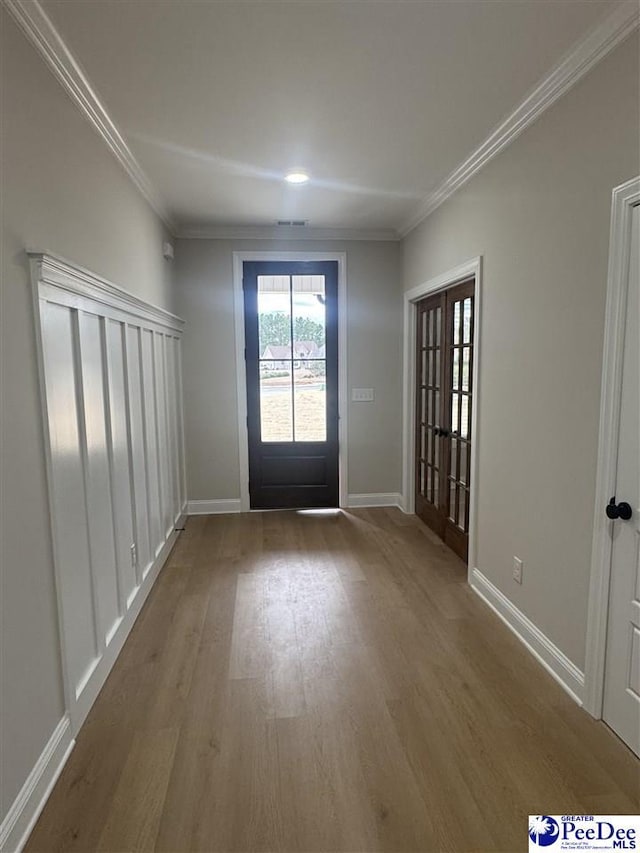 doorway with ornamental molding, wood finished floors, and baseboards