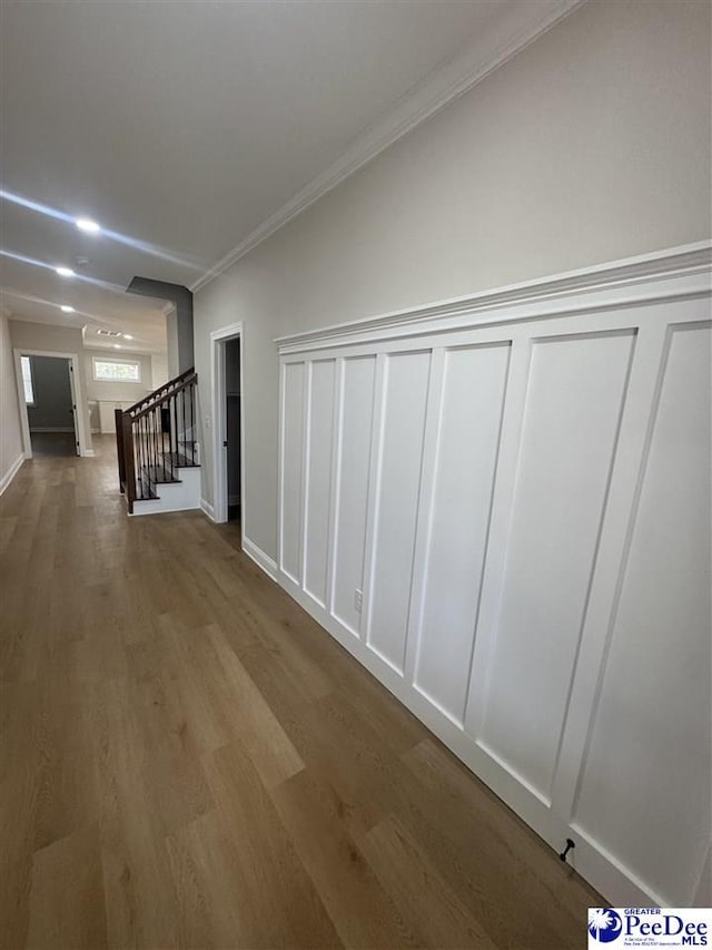 hall featuring stairs, ornamental molding, a decorative wall, and wood finished floors