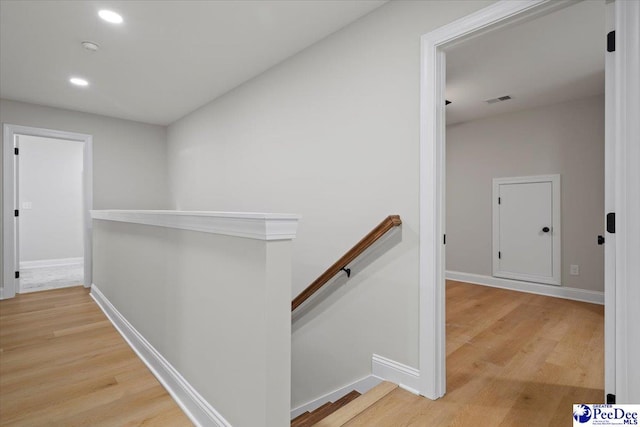 corridor featuring visible vents, wood finished floors, an upstairs landing, and baseboards