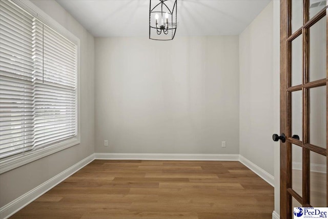 unfurnished room with baseboards, a notable chandelier, and light wood finished floors