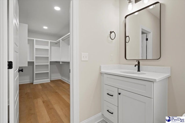 bathroom with recessed lighting, a spacious closet, vanity, wood finished floors, and baseboards