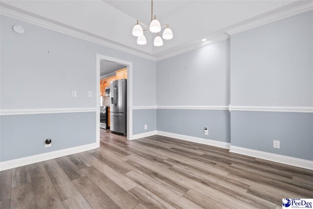 unfurnished room featuring an inviting chandelier, crown molding, wood finished floors, and baseboards