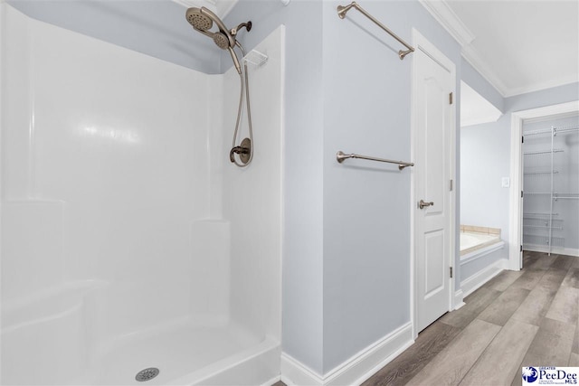 bathroom with a walk in closet, baseboards, crown molding, walk in shower, and wood finished floors