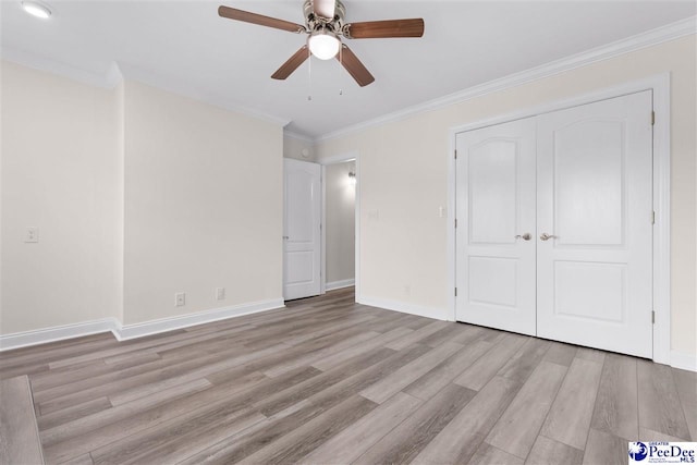 unfurnished bedroom featuring a closet, baseboards, wood finished floors, and crown molding