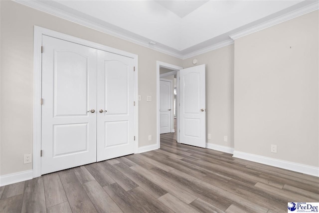 unfurnished bedroom featuring crown molding, wood finished floors, baseboards, and a closet