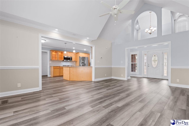 unfurnished living room with ceiling fan with notable chandelier, wood finished floors, visible vents, and baseboards