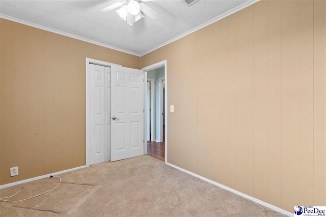 unfurnished bedroom featuring carpet, ceiling fan, baseboards, a textured ceiling, and crown molding