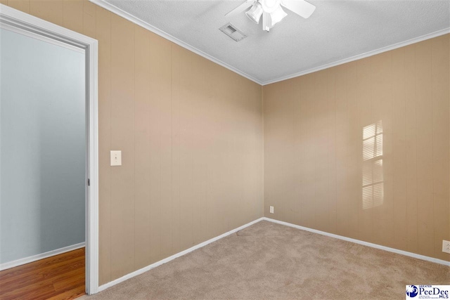 carpeted spare room featuring ornamental molding, ceiling fan, visible vents, and baseboards