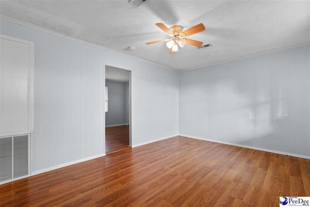 empty room featuring wood finished floors, visible vents, a ceiling fan, a textured ceiling, and crown molding