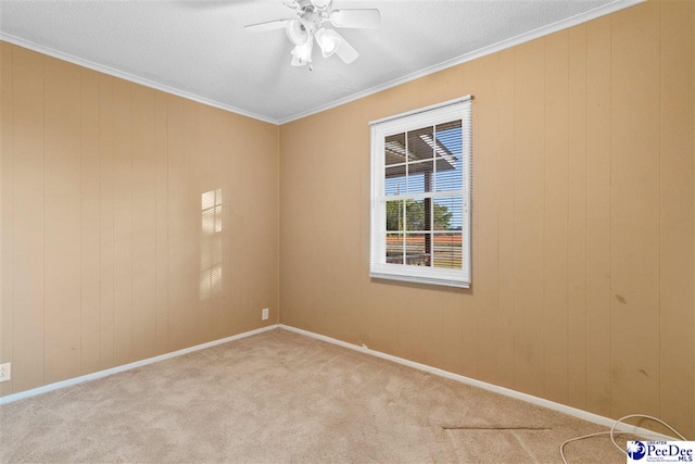 carpeted empty room featuring wooden walls, a ceiling fan, crown molding, and baseboards