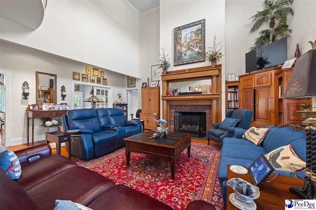 living room with crown molding, a towering ceiling, wood-type flooring, and a brick fireplace