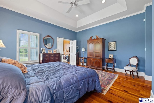 bedroom with dark hardwood / wood-style floors, ceiling fan, and a tray ceiling