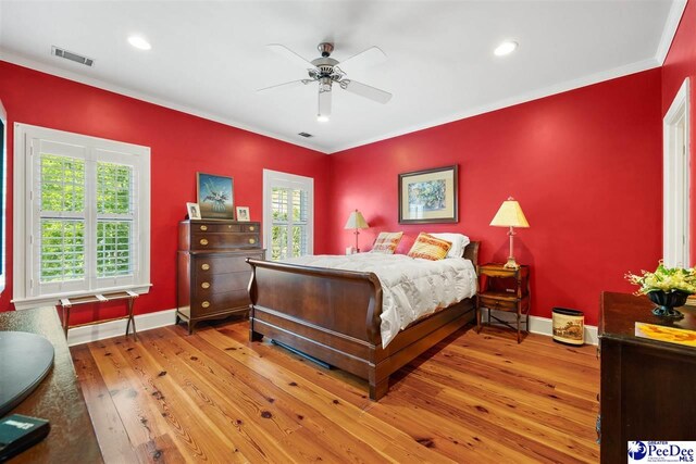 bedroom featuring hardwood / wood-style flooring, ceiling fan, crown molding, and multiple windows