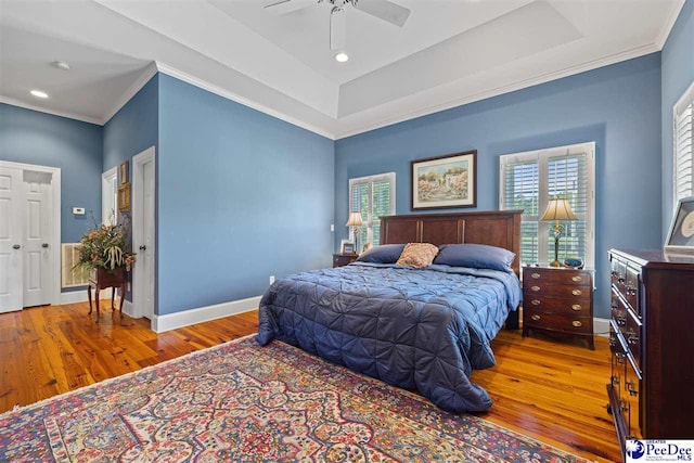 bedroom featuring a tray ceiling, hardwood / wood-style floors, and multiple windows