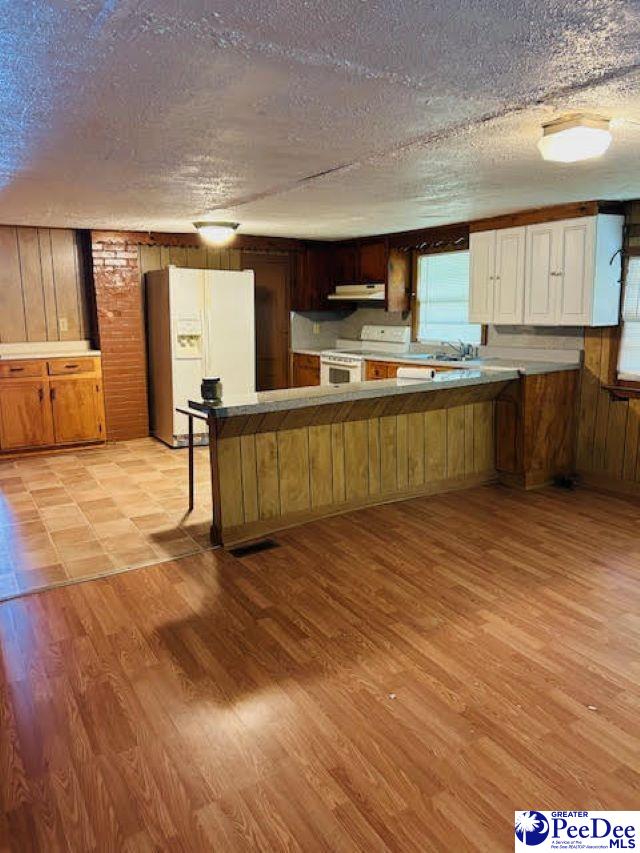 kitchen with a textured ceiling, wooden walls, kitchen peninsula, white appliances, and light hardwood / wood-style floors