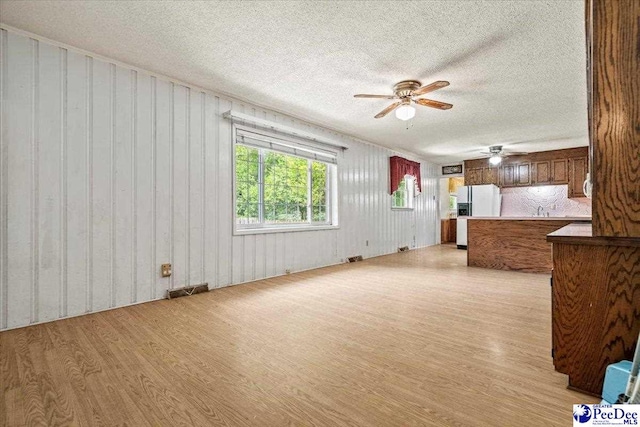 unfurnished living room featuring ceiling fan, sink, a textured ceiling, and light wood-type flooring