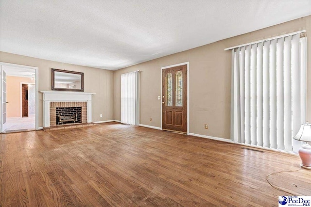 unfurnished living room featuring wood-type flooring, a brick fireplace, and a textured ceiling