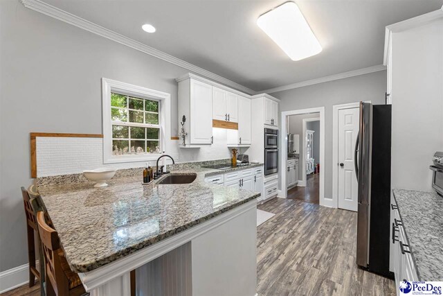 2409 Sarazen Ct, Florence, SC 29506 - kitchen featuring a sink, a peninsula, black appliances, white cabinets, and wood finished floors