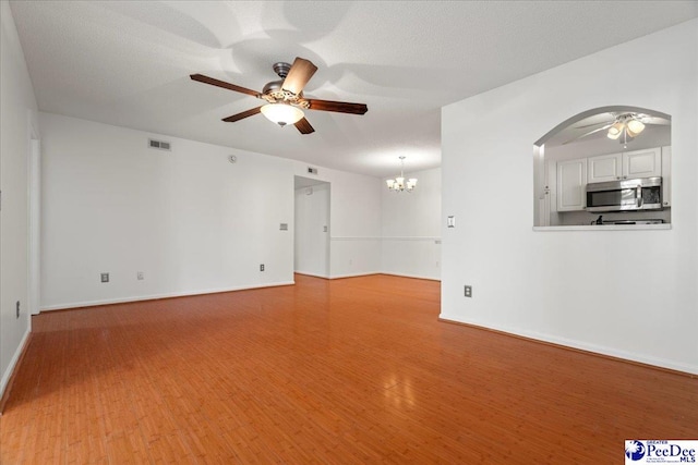 unfurnished living room featuring visible vents, light wood-style flooring, and ceiling fan with notable chandelier