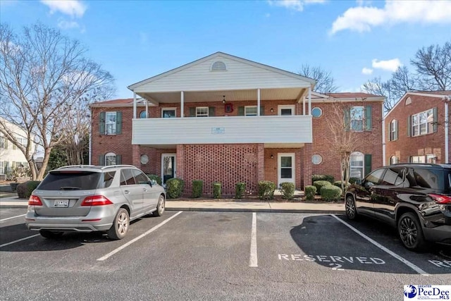 view of front facade featuring a balcony, uncovered parking, and brick siding