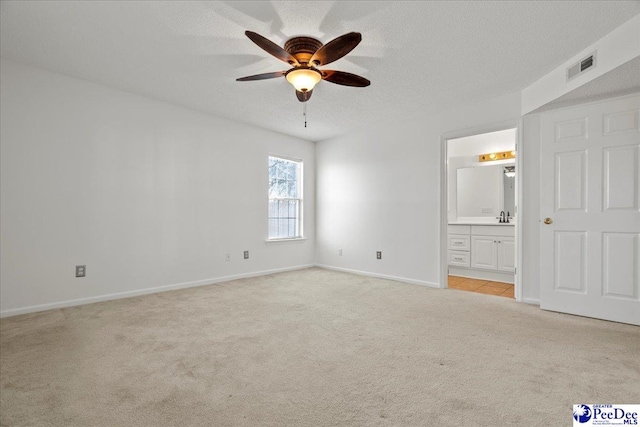 unfurnished bedroom featuring a textured ceiling, light carpet, a sink, visible vents, and baseboards