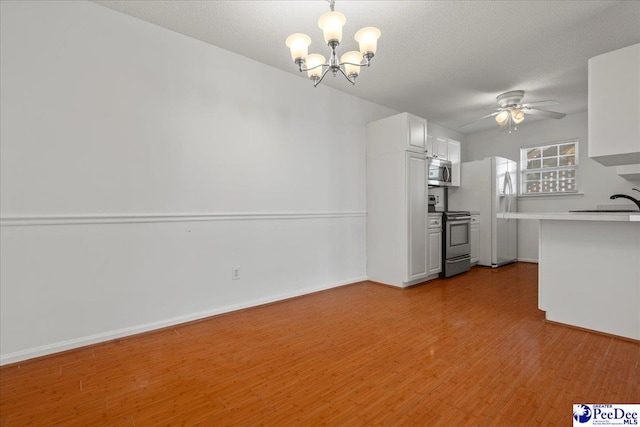 interior space featuring light wood finished floors, white cabinets, stainless steel appliances, light countertops, and ceiling fan with notable chandelier