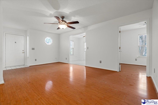 unfurnished living room with light wood-style floors, a textured ceiling, baseboards, and a ceiling fan