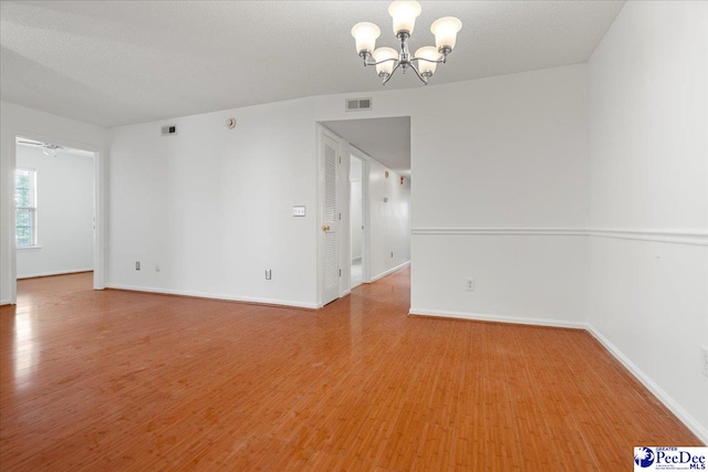 empty room featuring light wood finished floors, baseboards, visible vents, and a notable chandelier