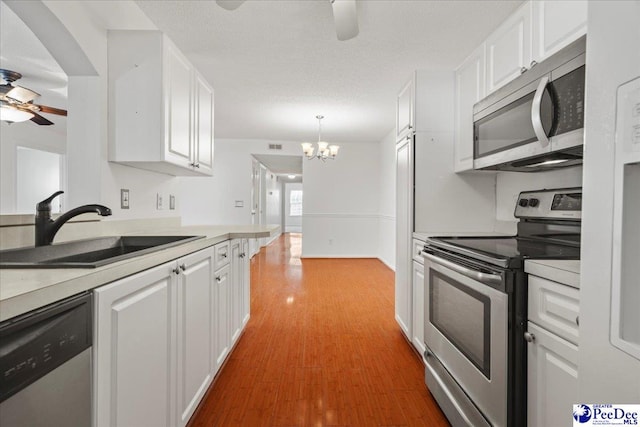 kitchen featuring appliances with stainless steel finishes, light countertops, white cabinetry, a sink, and ceiling fan with notable chandelier