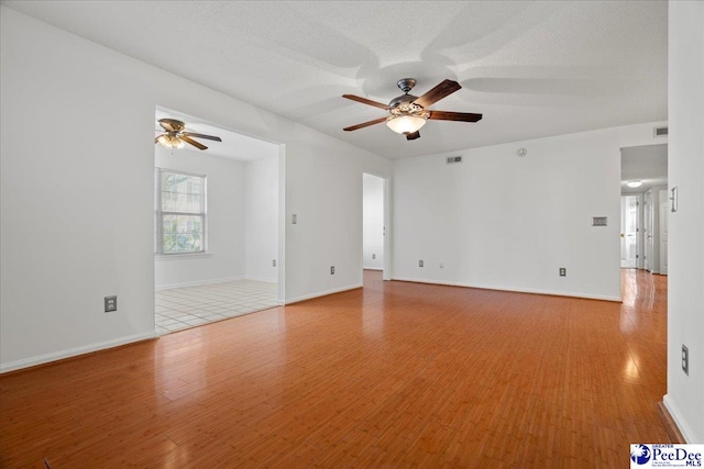 spare room with light wood-style floors, visible vents, a textured ceiling, and a ceiling fan