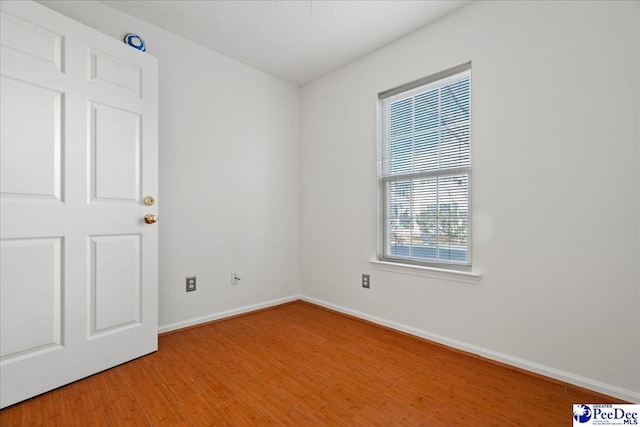 empty room with a textured ceiling, baseboards, and wood finished floors