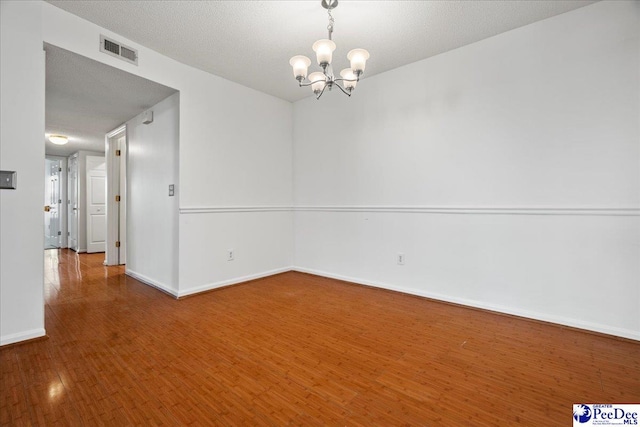 unfurnished room with a textured ceiling, a notable chandelier, visible vents, baseboards, and hardwood / wood-style floors