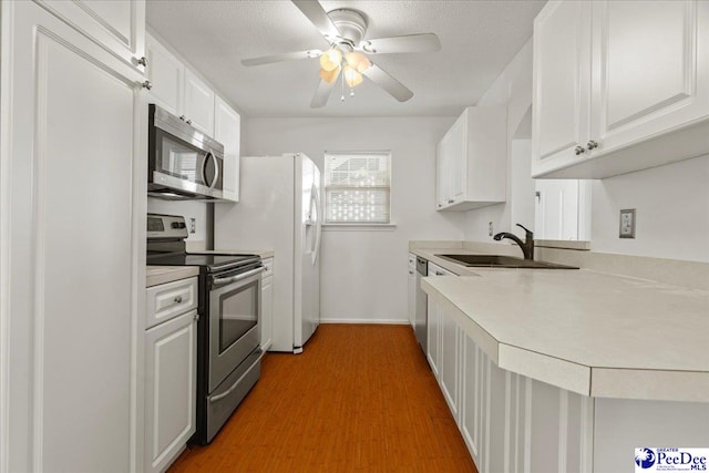 kitchen featuring white cabinets, appliances with stainless steel finishes, wood finished floors, light countertops, and a sink