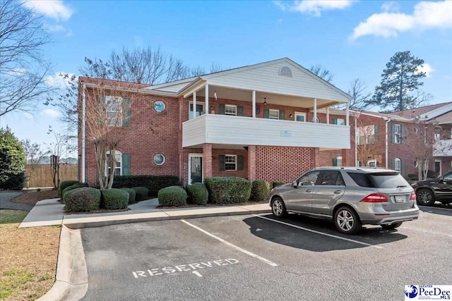 view of front of house featuring a balcony, uncovered parking, and brick siding