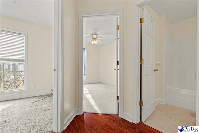 hall featuring a textured ceiling, wood finished floors, carpet flooring, and baseboards