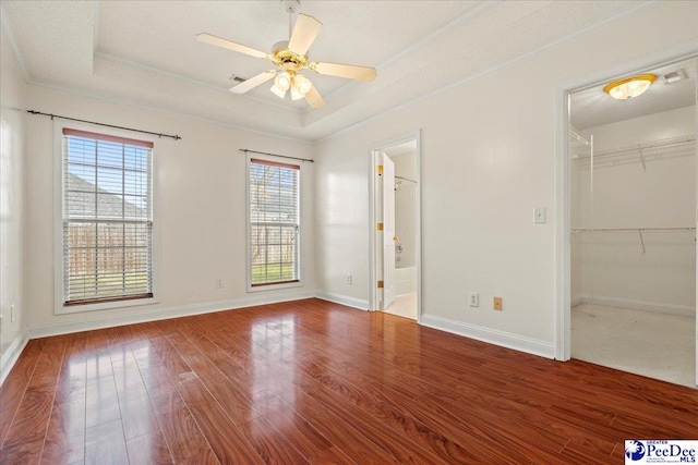 unfurnished bedroom with baseboards, wood finished floors, a tray ceiling, a walk in closet, and crown molding