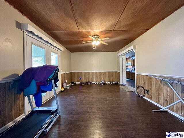 workout area featuring ceiling fan, wooden ceiling, dark hardwood / wood-style floors, and wood walls